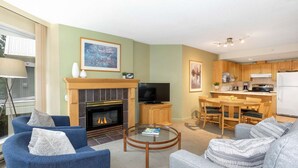 A living room with a fireplace, a television, and a dining area with wooden furniture. - Woodrun 306 - Ski in Ski out, Common Area Hot Tub, New Listing (Whistler)