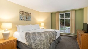 A hotel room with a bed, two bedside lamps, a painting, a television, and a window with curtains.