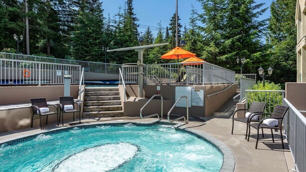 A swimming pool with steps leading down to it, surrounded by chairs and an umbrella. - Woodrun 306 - Ski in Ski out, Common Area Hot Tub, New Listing (Whistler)