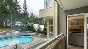 A residential building with a pool, a balcony with a view of trees and a lake, and a fireplace inside.
