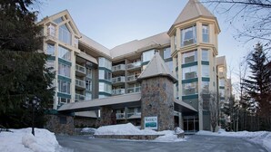 A multi-story hotel with a stone entrance, balconies, and a snow-covered ground. - Woodrun 306 - Ski in Ski out, Common Area Hot Tub, New Listing (Whistler)