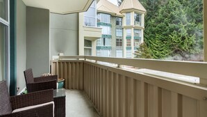 A balcony with wicker furniture and a view of a multi-story building with a turret. - Woodrun 306 - Ski in Ski out, Common Area Hot Tub, New Listing (Whistler)