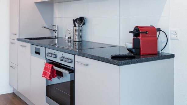A modern kitchen with white cabinetry, a built-in oven, a microwave, and a coffee maker. - Apartment  by Interhome (Zurich)