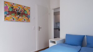 A bedroom with a bed, a nightstand, a door, and a colorful painting on the wall. - Apartment  by Interhome (Zurich)