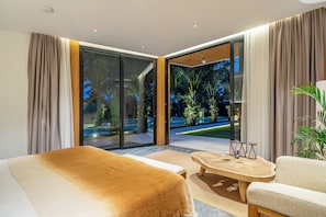 Ein modernes Hotelzimmer mit einem großen Bett, einem Holztisch und Blick auf einen angelegten Garten durch Glastüren.