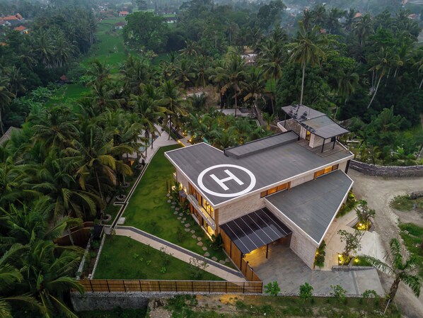 Un edificio moderno con un llamativo logotipo 'H', rodeado de exuberante vegetación y palmeras.