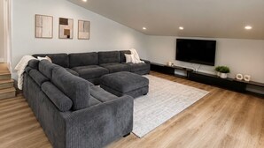 Una sala de estar moderna con un sofá seccional, un televisor de pantalla plana e iluminación empotrada en el techo.