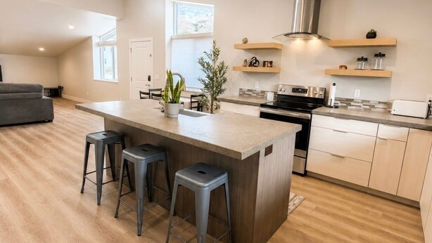 Una cocina moderna con una isla central, taburetes de bar, estufa y estanterías empotradas.