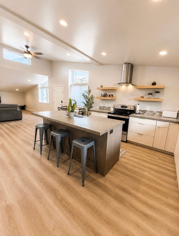 A modern kitchen with a central island, bar stools, a stove, and built-in shelves. - Modern and Cozy Retreat (Pleasant Grove)