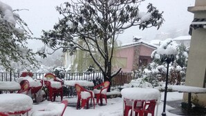 Outdoor seating with red chairs covered in snow, a tree, and a building in the background. - Hotel Alto de las Estazadas (Cabrales)