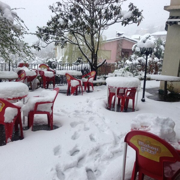 Outdoor seating with red chairs covered in snow, a tree, and a building in the background. - Hotel Alto de las Estazadas (Cabrales)