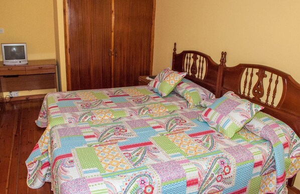 A bedroom with a wooden bed, a wooden nightstand, a television on the nightstand, and a wooden wardrobe. - Hotel Alto de las Estazadas (Cabrales)