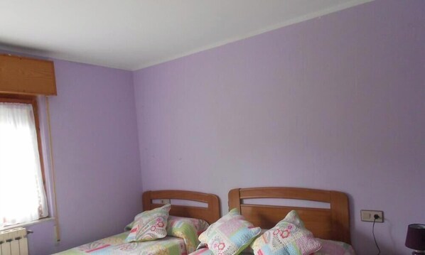A room with two wooden beds, a window with curtains, and a wall socket. - Hotel Alto de las Estazadas (Cabrales)