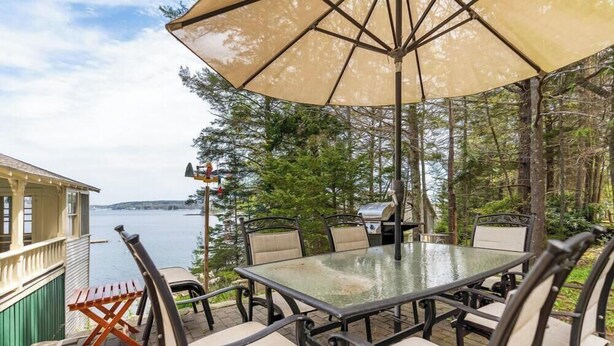 An outdoor dining area with a glass table, chairs, and a large umbrella. - Charming 4BR, 2BA Southport retreat for up to 8 guests. (Southport)