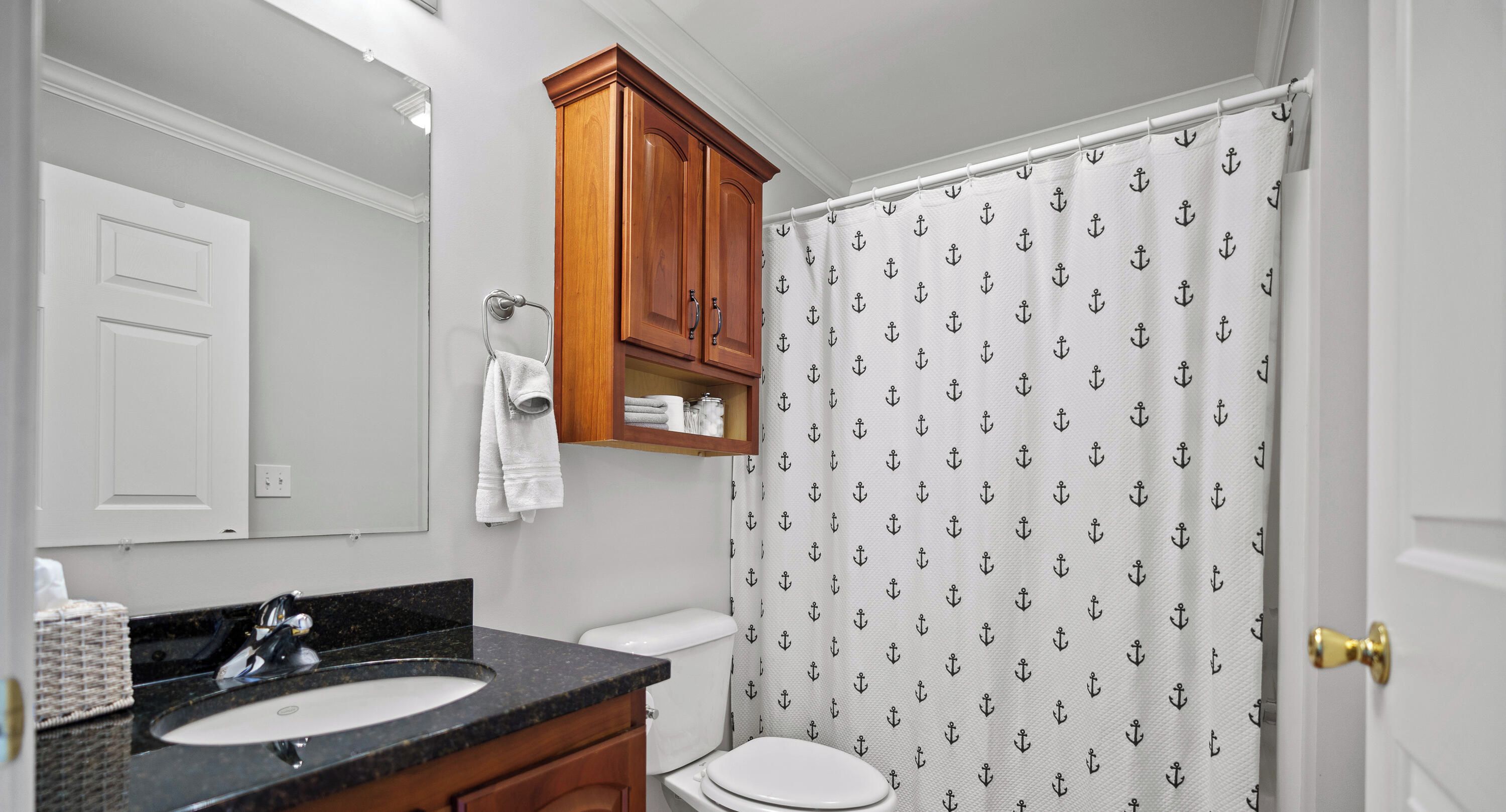 A bathroom with a white sink, wooden vanity, and a shower curtain with anchor patterns.