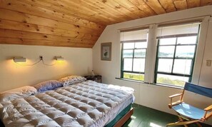 Ein Schlafzimmer mit einem Bett, zwei Nachttischlampen, einem Fenster und einer Holzbalkendecke.