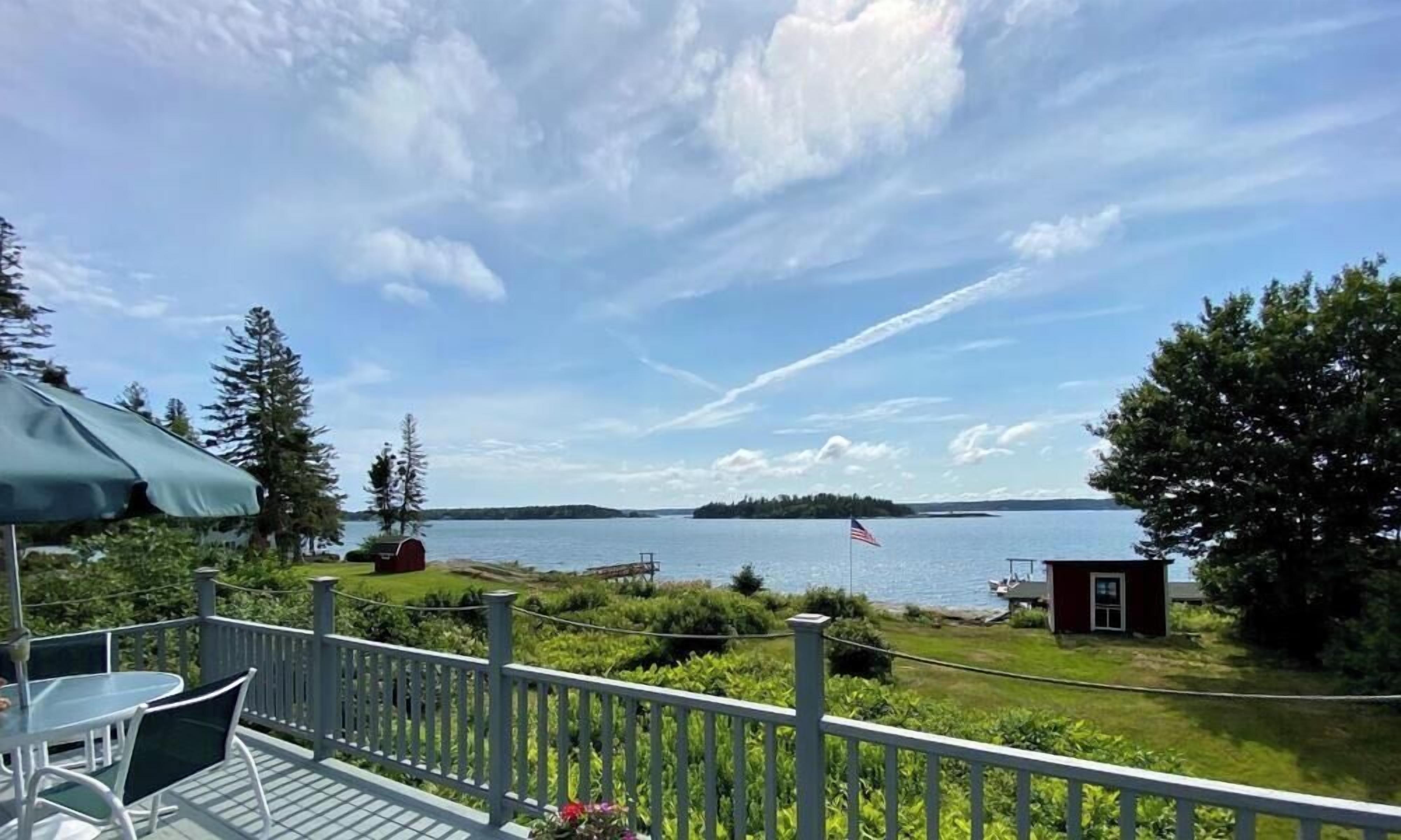 A deck with a view of a lake, a small shed, and a flag.