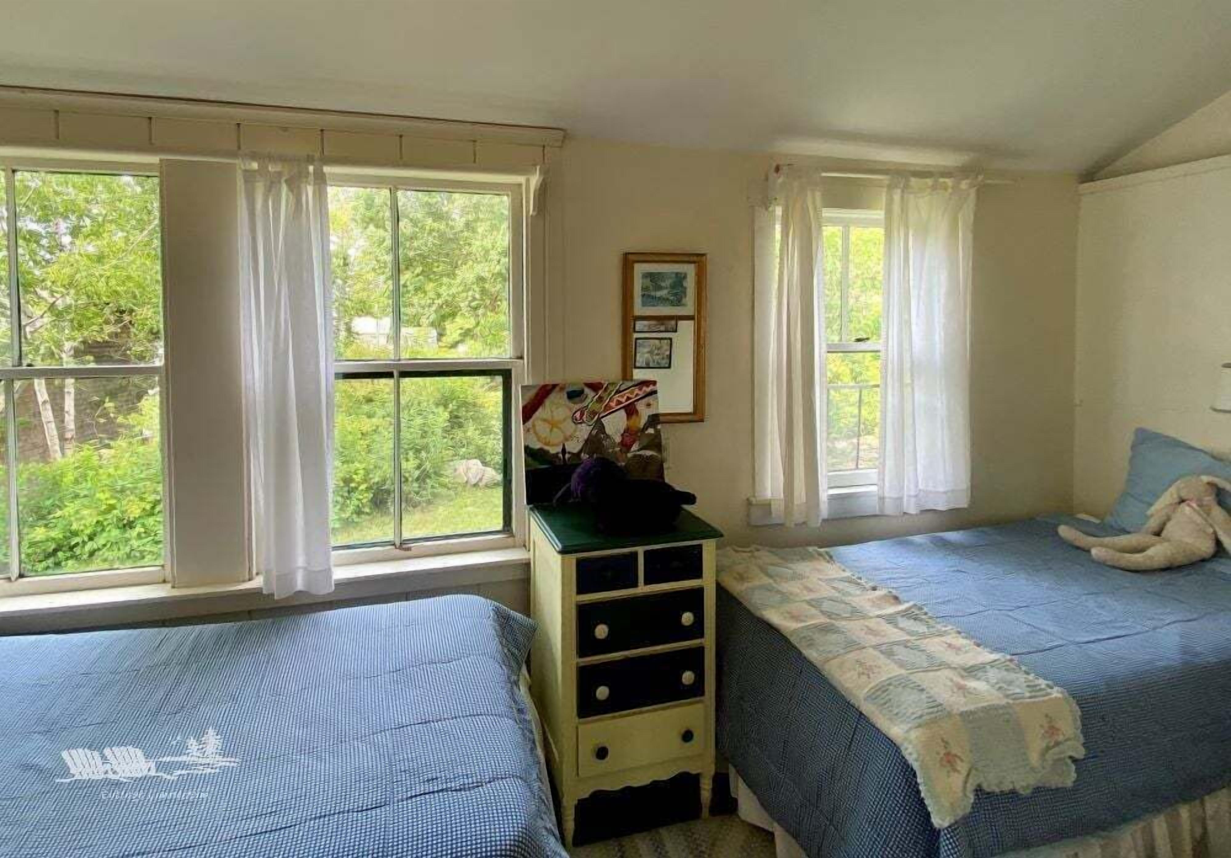 A room with two beds, a dresser, and large windows with curtains.