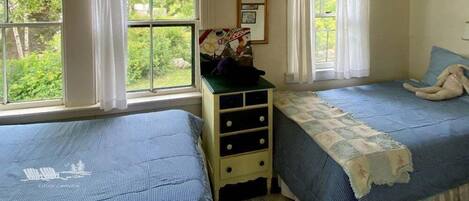 A room with two beds, a dresser, and large windows with curtains.