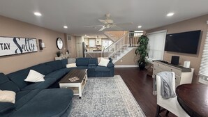 A living room with a sectional sofa, a coffee table, a rug, a TV, and a staircase leading to a kitchen. -  4 bedroom + bonus room house  with ocean view in Sea Isle City (Sea Isle City)
