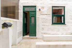 A white stone building with a green door and window, a mailbox, and a small step leading to the entrance. - GuestReady - Trendy House (Porto)