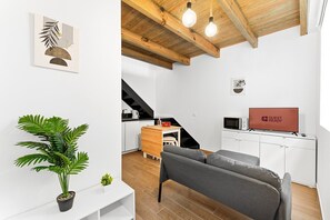 A modern living room with a sofa, a dining area with a table and chairs, a kitchen with a microwave, and a staircase. - GuestReady - Trendy House (Porto)