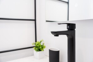 A modern bathroom with a black faucet, a white sink, and a small potted plant. - GuestReady - Trendy House (Porto)