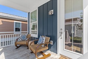 Une véranda avec deux fauteuils à bascule, une balustrade blanche et une porte bleu foncé.