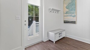 Ein Zimmer mit weißer Tür, einer Bank, einem Kleiderständer und einem Bild an der Wand.