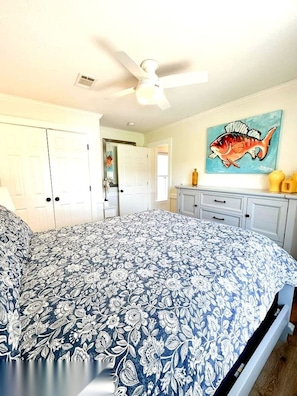 Een slaapkamer met een bed, een plafondventilator, een schilderij van een vis en een witte inloopkast.