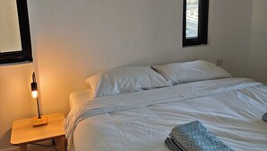 Quarto com cama, mesa de cabeceira, abajur, janela e vista exterior.