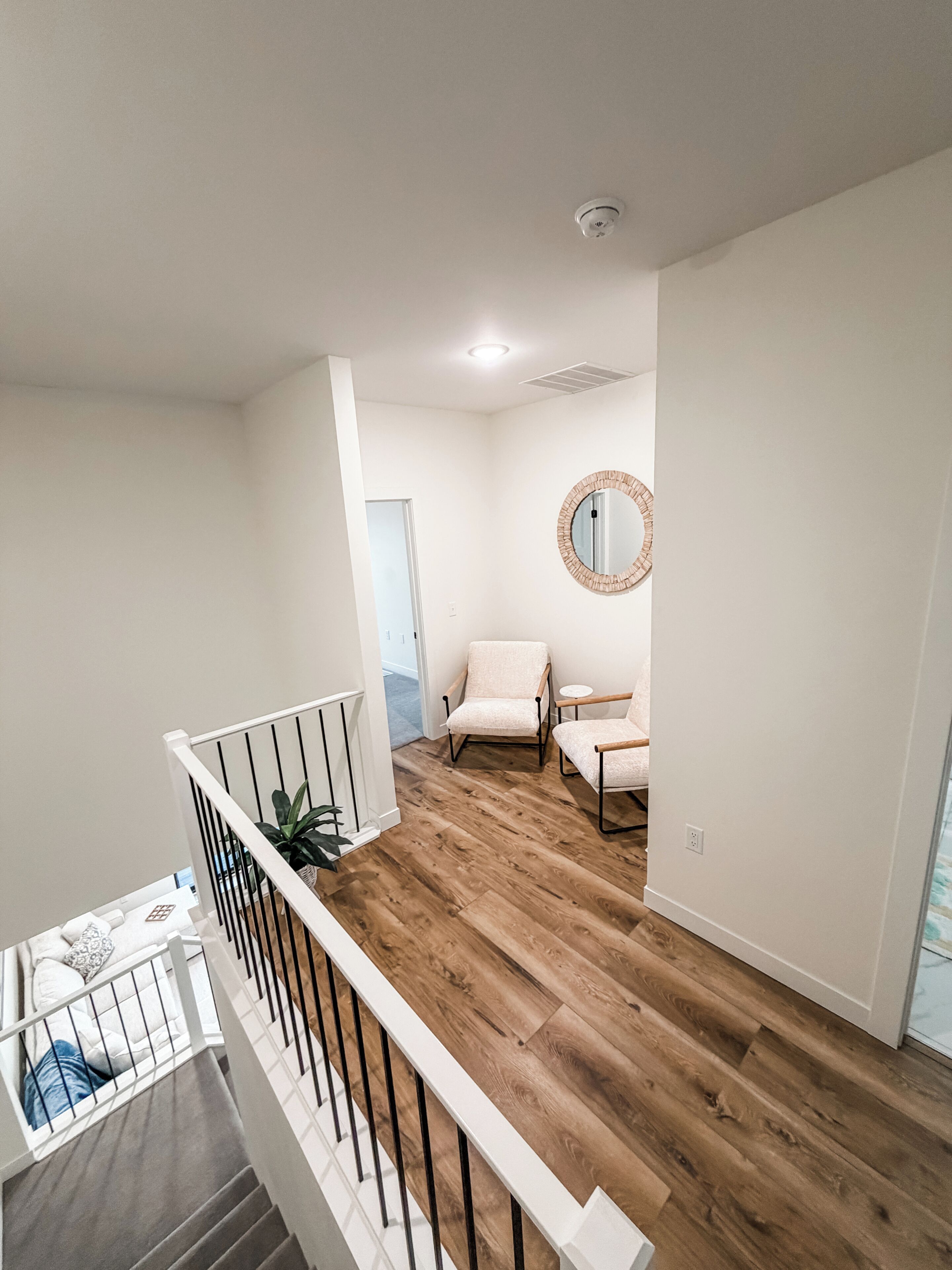 A modern interior with a wooden floor, white walls, a round mirror, and a staircase.