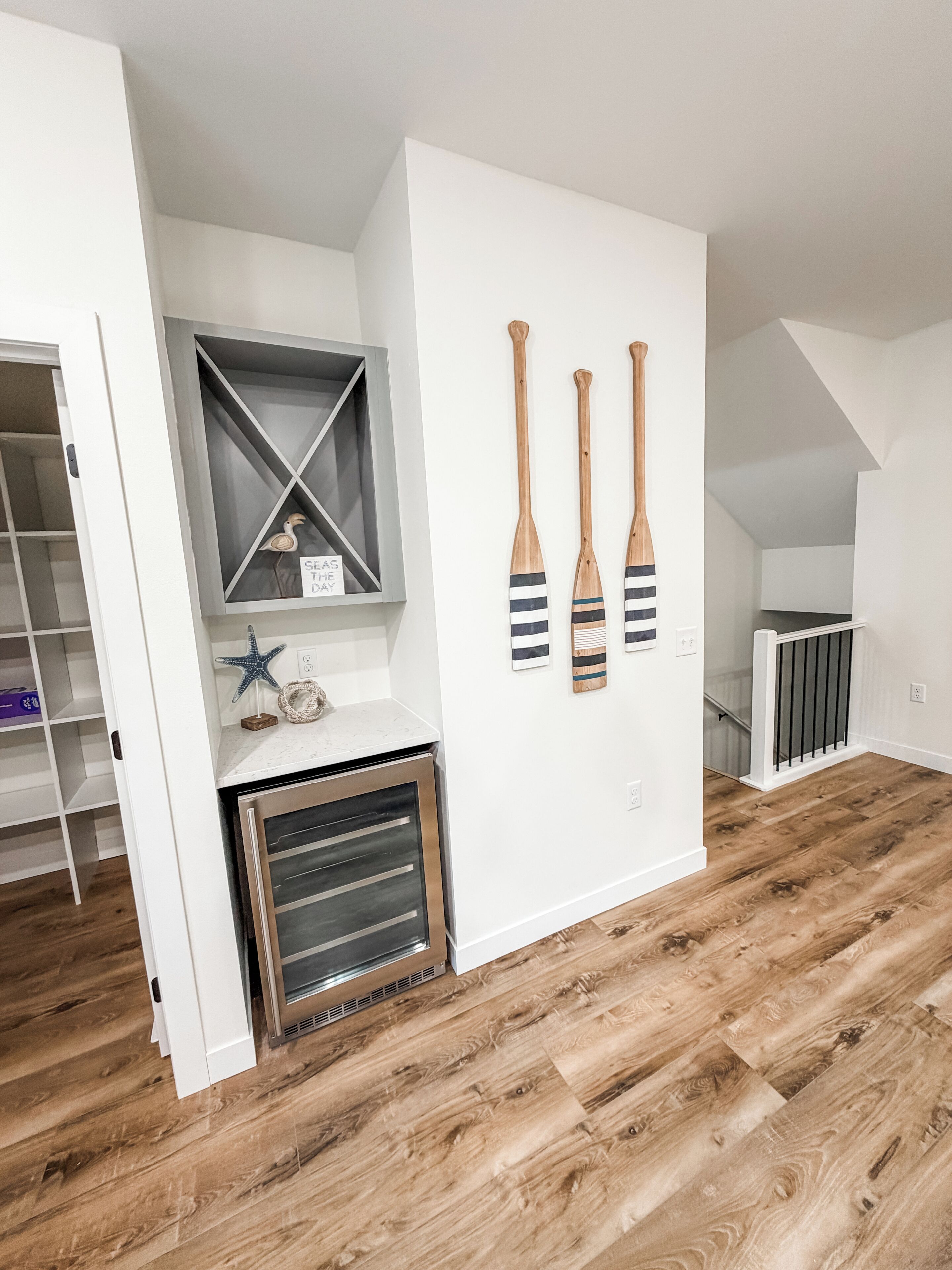 Un intérieur moderne avec un plancher en bois, un four encastré, un mur blanc agrémenté d’une étagère et trois pagaies en bois.