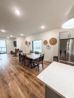 Eine moderne Küche mit einem Edelstahl-Kühlschrank, einem Holzespeisetisch und Stühlen, mit einem großen Fenster für natürliches Licht.