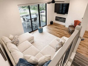Ein modernes Wohnzimmer mit Ecksofa, Essbereich mit Tisch und Stühlen, einem an der Wand befestigten Fernseher und Blick ins Freie.