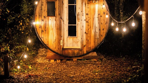 A wooden cabin with a door, a window, and a chimney. - The Pine Loft Bunkie (Lac du Bonnet)