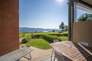 Eine Terrasse mit Tisch und Stühlen, eine Ziegelwand und Blick auf eine grüne Landschaft mit Bergen in der Ferne.