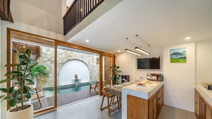 A modern kitchen with a stone wall, a dining area with a pool view, and a TV mounted on the wall. - A9 Bali Dream Villa (Kerobokan)