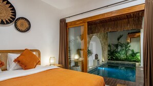 A hotel room with a bed, a nightstand, a lamp, a large window with a view of a pool and greenery. - A9 Bali Dream Villa (Kerobokan)
