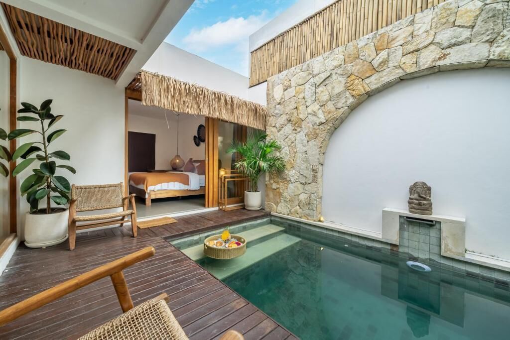 Area piscina con muro in pietra, veranda in legno e un letto visibile attraverso una porta in vetro.