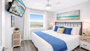 A bedroom with a bed, a TV mounted on the wall, a ceiling fan, a window with a view, and a painting on the wall. - Beach View Plantation 4515 With Multiple Resort Amenities (Gulf Shores)
