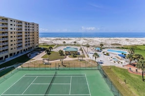 Un hotel con varios pisos, una cancha de tenis y una zona de piscina con vista a la playa.