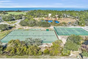 Vista aérea de un complejo de canchas de tenis rodeado de vegetación densa y una masa de agua.