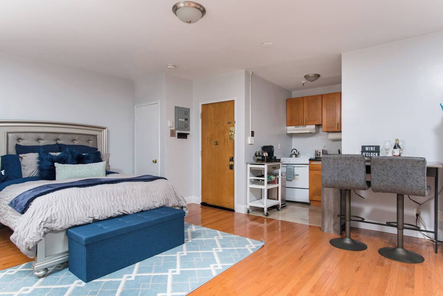 A bedroom with a bed, a bench, a kitchenette, and a small bar area.