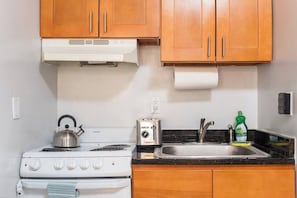 Una cocina compacta con estufa, tostadora, fregadero y armarios de madera.