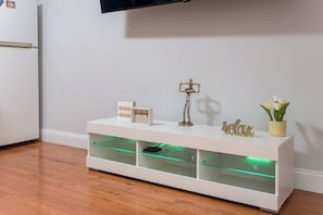Un mueble blanco de entretenimiento con estantes, una pequeña estatua, un cartel y un jarrón con flores.