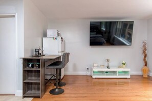 Een moderne woonkamer met een flatscreen televisie, een houten eettafel met barstoelen, een witte tv-kast en een vaas met een plant.