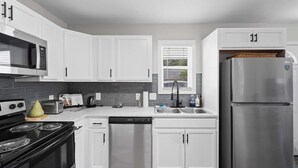 Una cocina moderna con armarios blancos, un refrigerador de acero inoxidable, un microondas, una estufa y un lavavajillas.