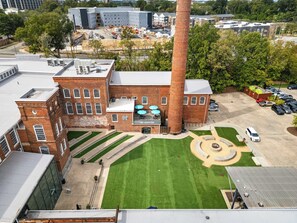 A large brick building with a prominent chimney, a parking lot, and a well-maintained lawn. - 7 Min Walk to Golden Belt | 8 Min to Hospital (Durham)