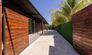 A narrow pathway flanked by wooden walls and a green fence, leading to a building with a metal roof.